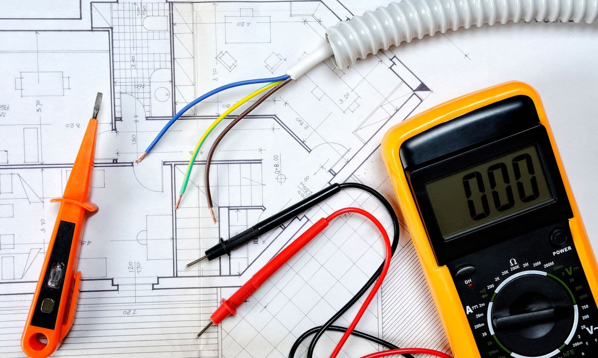 Electrical plans on a workbench with a multimeter, level and wiring