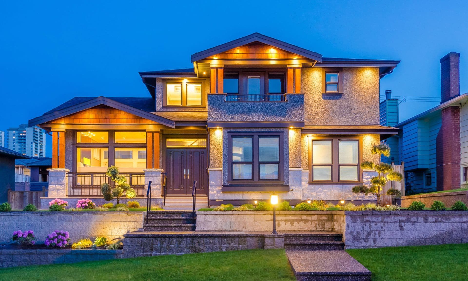 A large home at dusk with its porch, path and window lights on